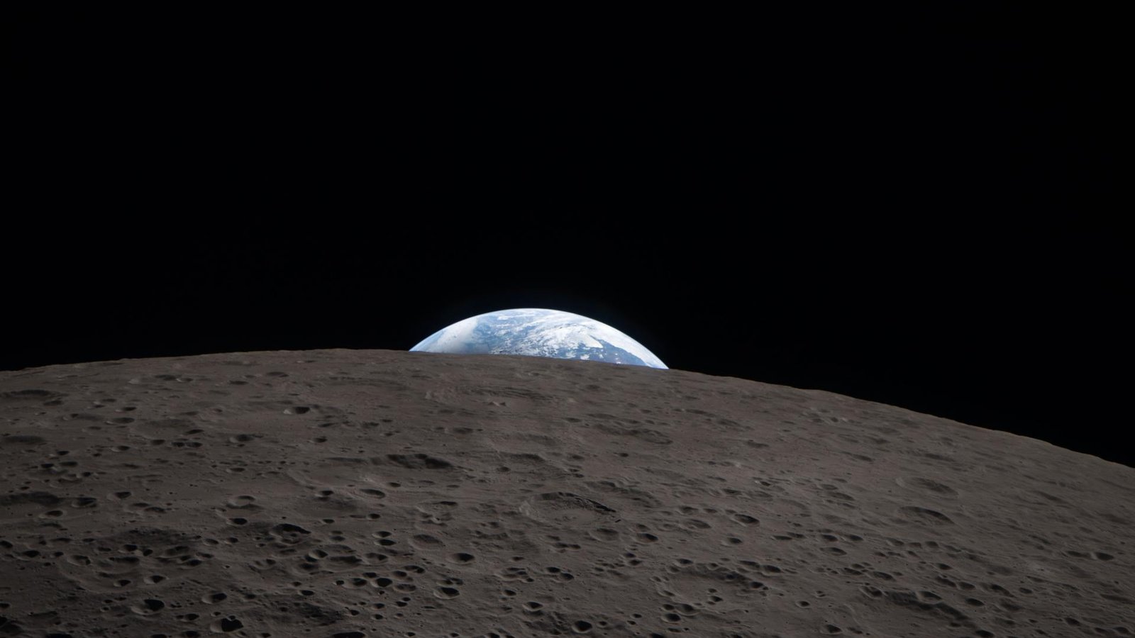 Earth, partly lit, sets behind the grey cratered horizon of the Moon's far side, photographed from the Orion spacecraft
