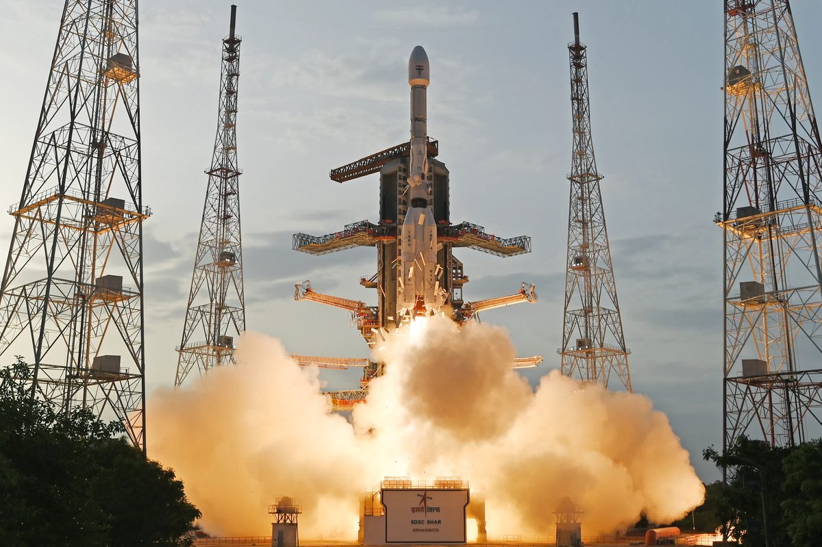 A GSLV rocket rising off its pad at Sriharikota on a cloud of exhaust, between tall lightning towers