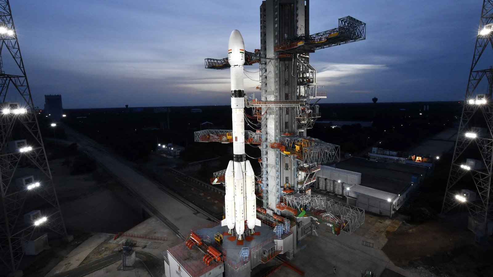 ISRO's GSLV-F17 rocket standing on the Second Launch Pad at Sriharikota at dusk, beside its service tower, with floodlight towers on each side