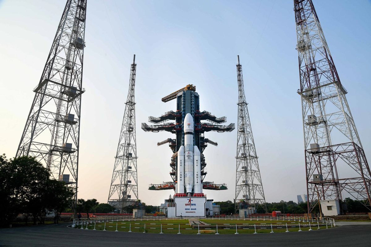 An LVM3 rocket, white with two large side boosters, standing on its launch pad at Sriharikota between four tall lightning towers