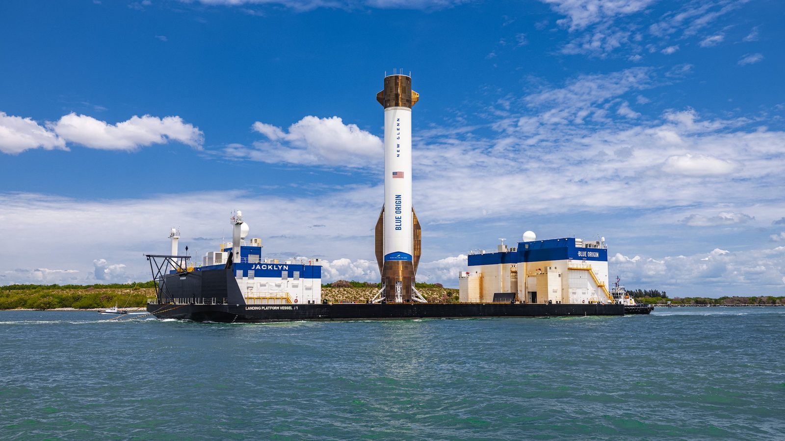 A white and copper-coloured New Glenn first stage stands upright on the deck of Blue Origin's landing ship Jacklyn as it sails back to Florida under a blue sky