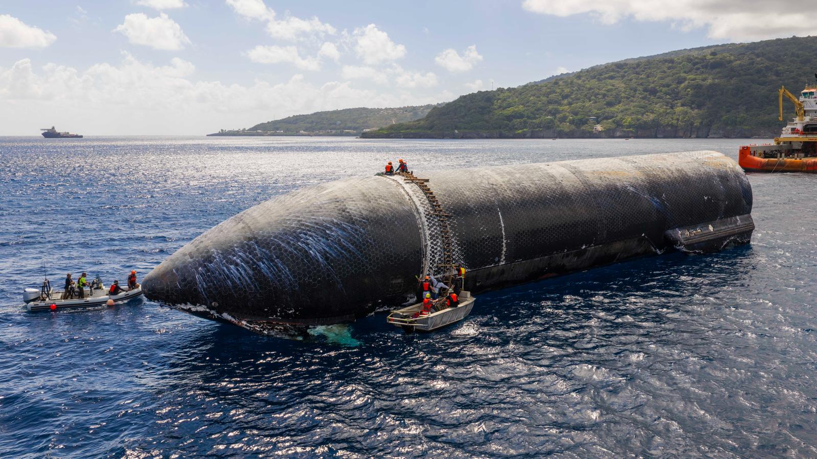 Ship 40, the Flight 13 Starship, floating on its side in calm blue water off Christmas Island, its black heat-shield tiles facing up, with SpaceX crews in small boats and a ladder against its side