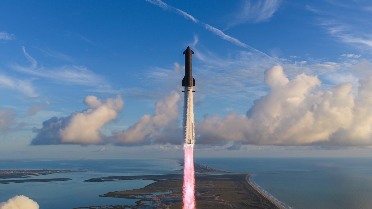 The full Starship stack climbing above the Starbase coastline on a column of exhaust, with the booster below and the ship on top