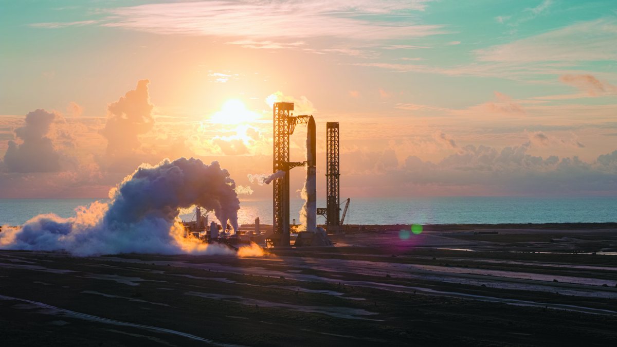 Starship lifting off at sunrise from Starbase, a small silhouette between the two launch towers with the low sun behind it and exhaust clouds rolling across the pad