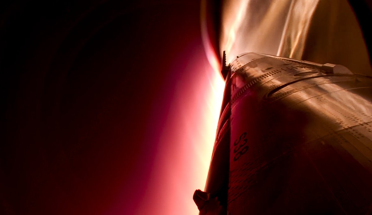 View from a camera on the ship looking along its side, with a red-orange glow of reentry heating at the edge of the frame