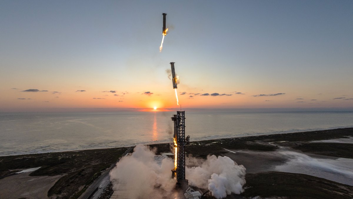 A view from high on a launch tower at sunrise, showing Starship climbing away and the Super Heavy booster descending towards the tower